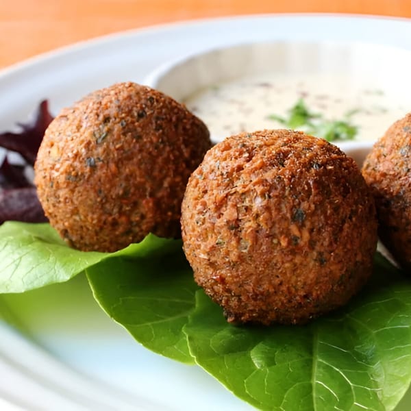 Three golden-brown falafel balls on lettuce leaves with a side of creamy tahini sauce.