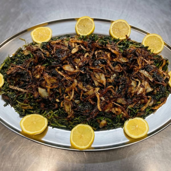 A large oval platter of green stewed greens topped with crispy fried onions and lemon slices.